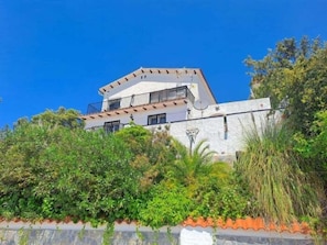 A two-story building with balconies, surrounded by greenery.