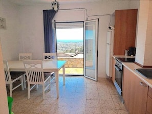 A small kitchen with a dining area, a view through a glass door, and a balcony.
