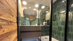 A modern bathroom with a wooden panel wall, a glass shower enclosure, and a vanity with a mirror. - Chalet le Nutshell - AravisTour (Thônes)