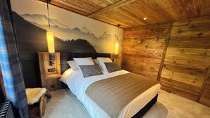 Une chambre confortable avec un plafond en bois, un lit recouvert de draps blancs et une fresque représentant une montagne sur le mur.