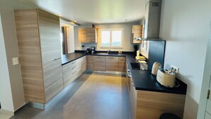 A modern kitchen with wooden cabinets, a black countertop, and a built-in oven. - Bellevue Spéra (Spéracèdes)