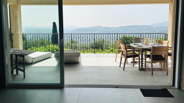 A balcony with a table set for dining, a sofa, and a view of the countryside. - Bellevue Spéra (Spéracèdes)