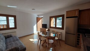 A compact kitchen with a dining table, chairs, a refrigerator, and a TV on a wooden cabinet. - Rural House with authentic apartments 1.340m, with garden, bbq and terrace (Senet)