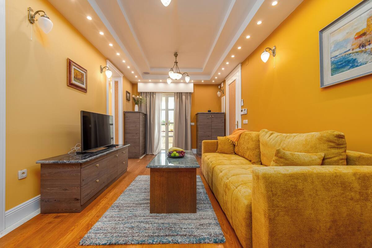 A living room with a sofa, TV, wooden cabinet, and a dining table with fruit.