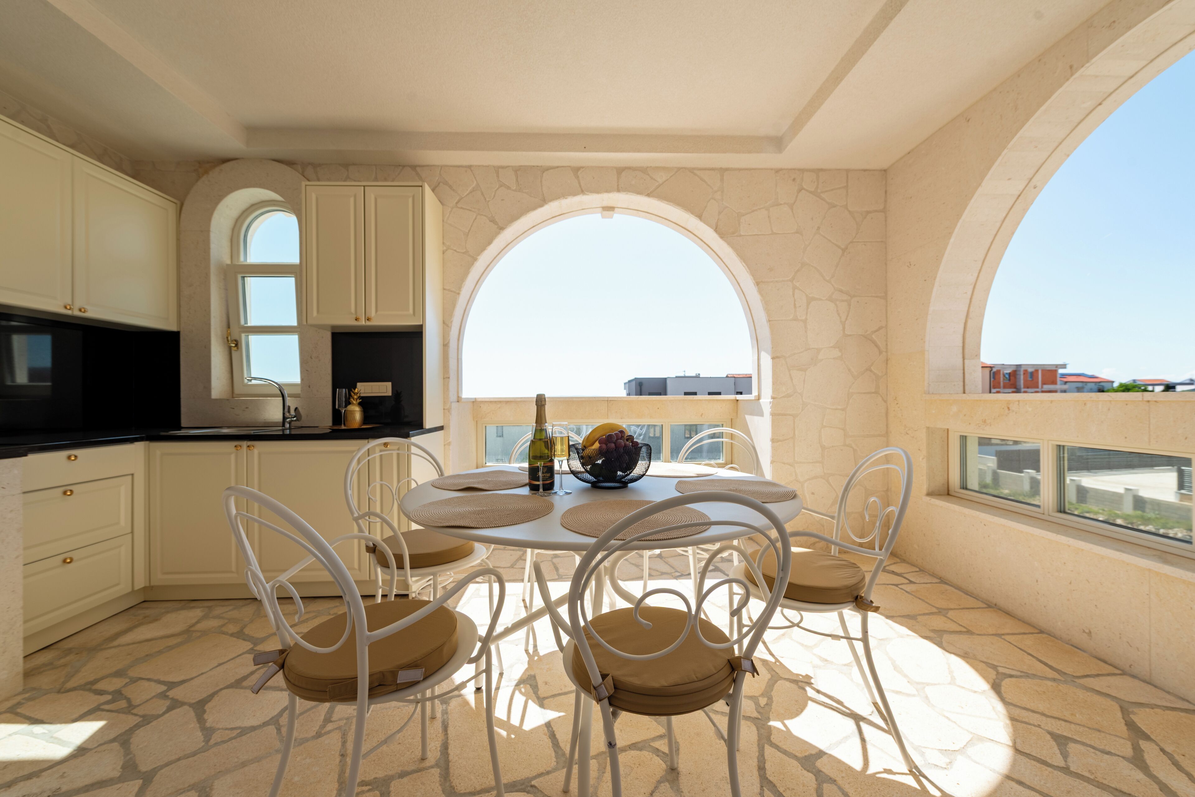 A dining area with a round table, white chairs, and a view through arched windows.
