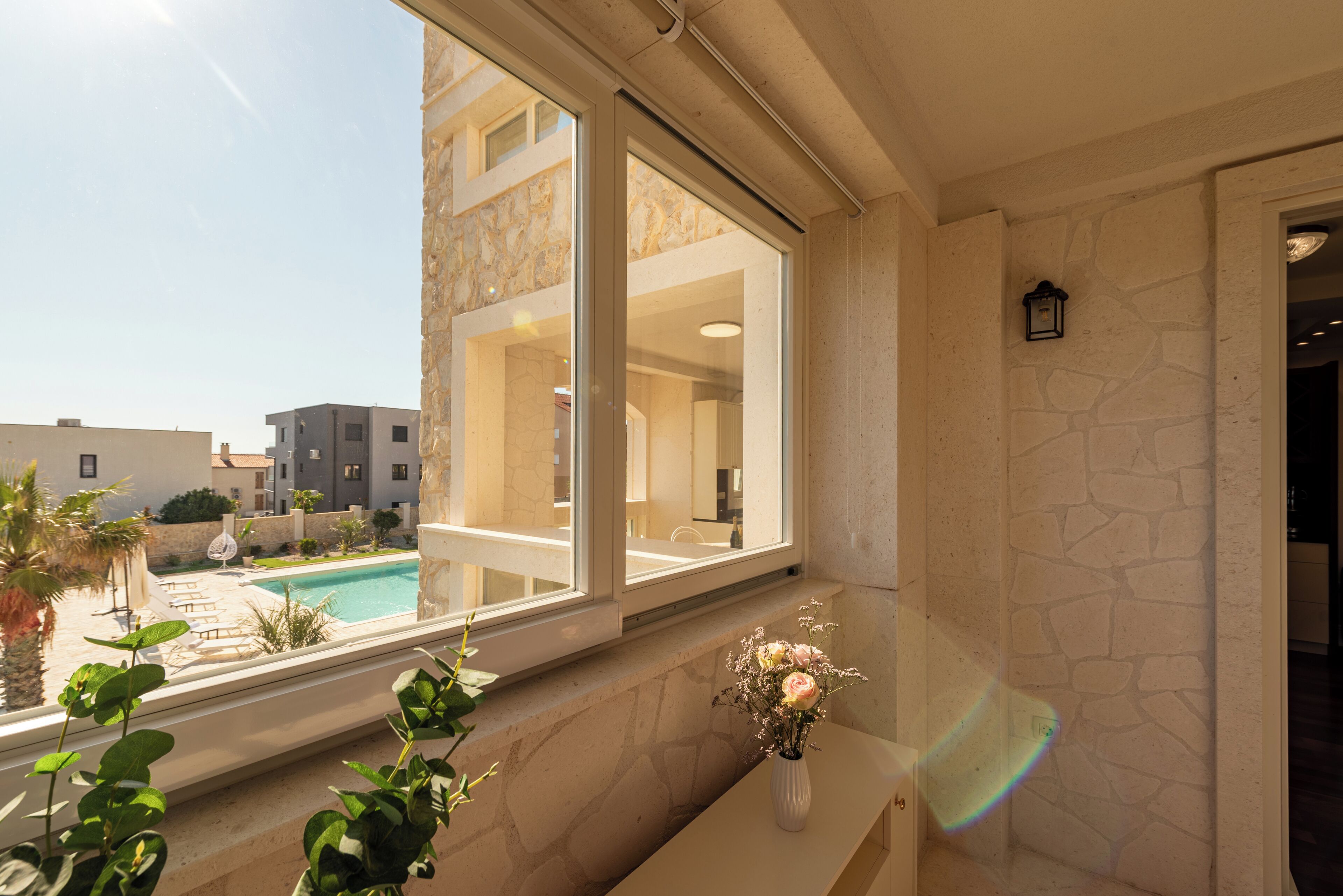 A modern bathroom with a large window, a stone wall, and a vase with flowers on a bench.