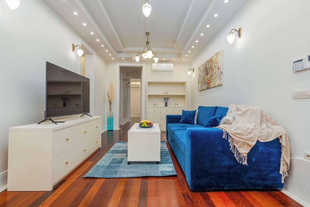 A modern living room with a blue sofa, white entertainment unit, and a flat-screen TV.