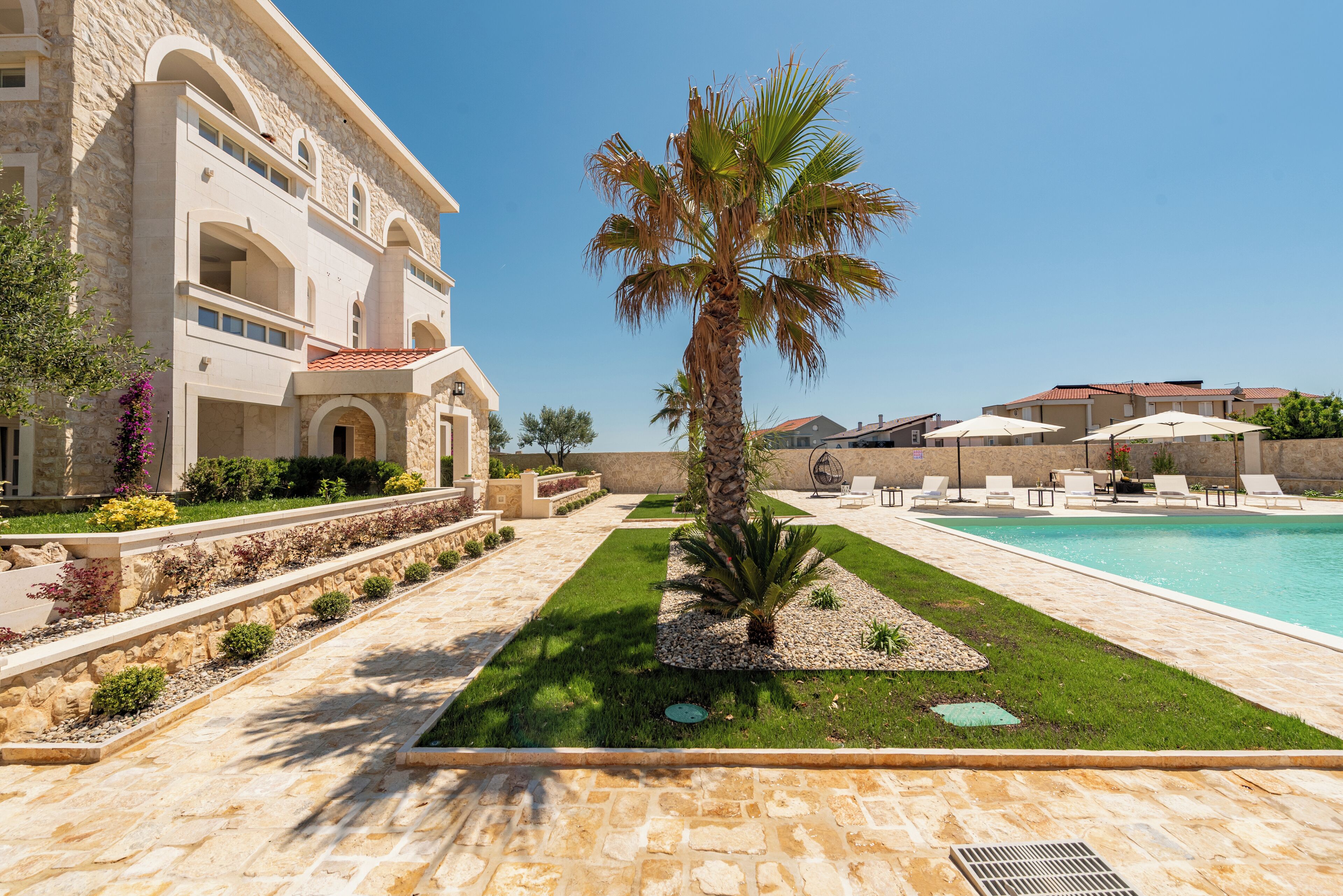 A poolside area with a palm tree, lounge chairs, and a stone building with arches.
