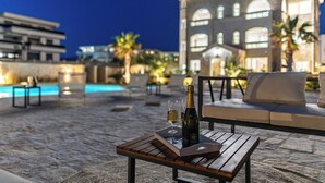 A poolside area with a wooden table, a bottle of champagne, and glasses. There are lounge chairs and a building with arched windows in the background. - Chateau Dabo (Novalja)