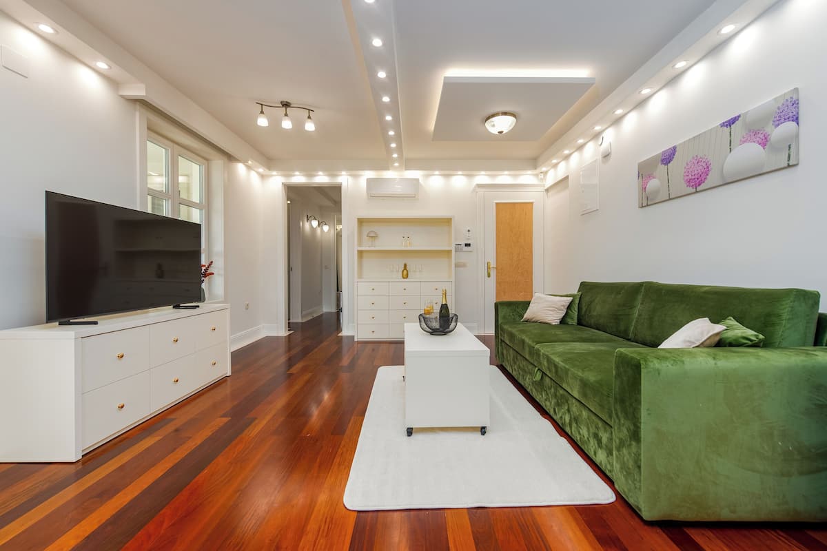 A modern living room with a flat-screen TV, a green sofa, and a white coffee table.