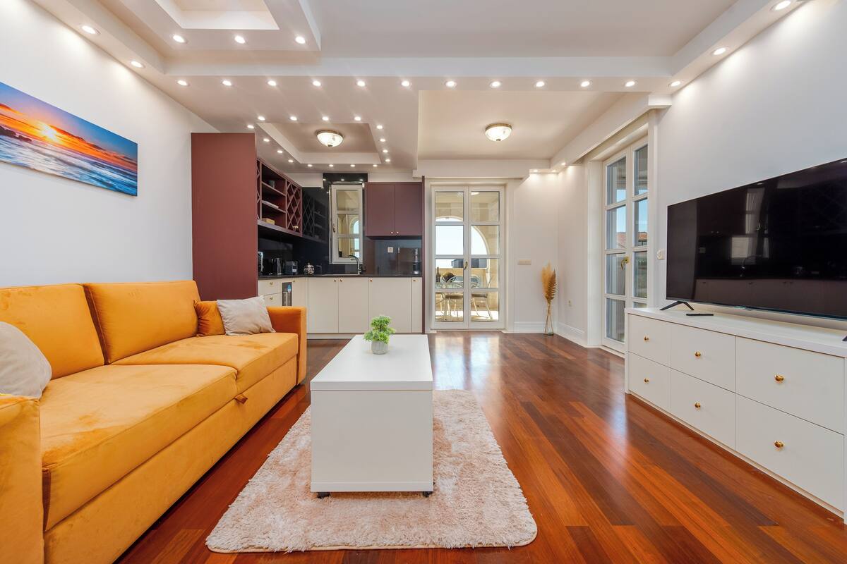 A modern living room with a sofa, coffee table, TV, and kitchen area.
