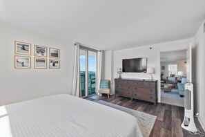 A bedroom with a bed, a dresser, a TV, and a balcony with curtains.