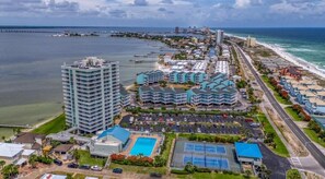 A coastal hotel with multiple buildings, a swimming pool, tennis courts, and a parking lot.