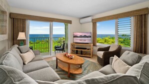 Een ruime woonkamer met een grote flatscreen televisie, comfortabele zithoek en een balkon met uitzicht op zee.