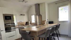 A modern kitchen with a central island, bar stools, a built-in oven, and a large window.