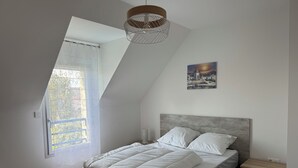 A bedroom with a sloped ceiling, a bed with white bedding, a nightstand, and a painting on the wall.