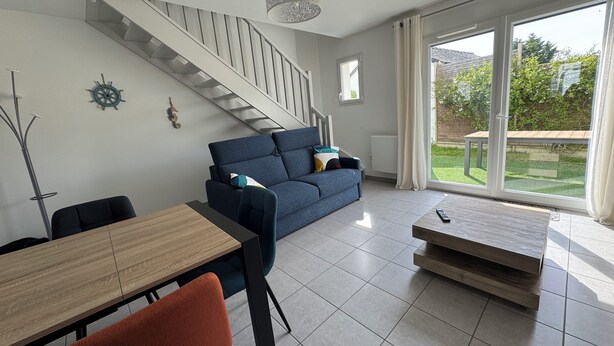 A modern living room with a staircase, a dining area, and a large sliding glass door to the outdoors.