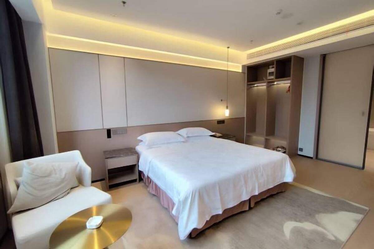 A modern hotel room with a bed, bedside table, and a seating area with a chair and a small table.
