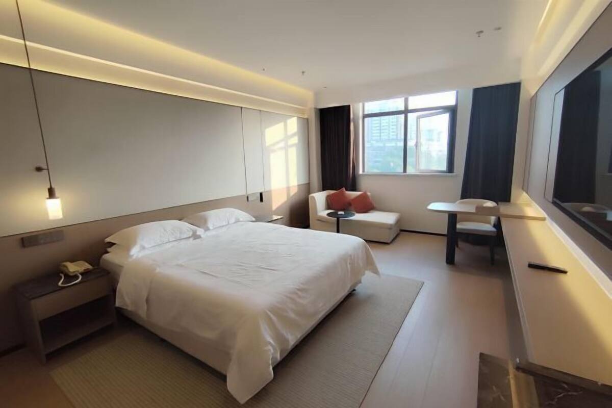 A modern hotel room with a large bed, bedside table, and a desk with a chair.