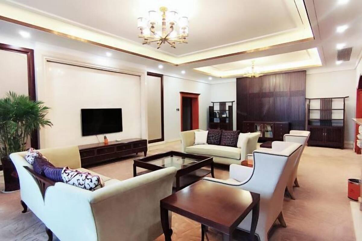 A spacious living room with a flat-screen TV, a chandelier, and a large wooden panel wall.
