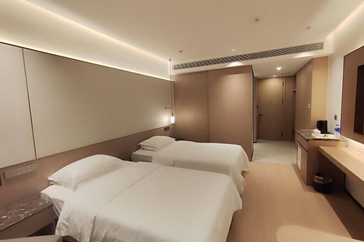 A hotel room with two beds, a desk, a mirror, and a kitchenette.
