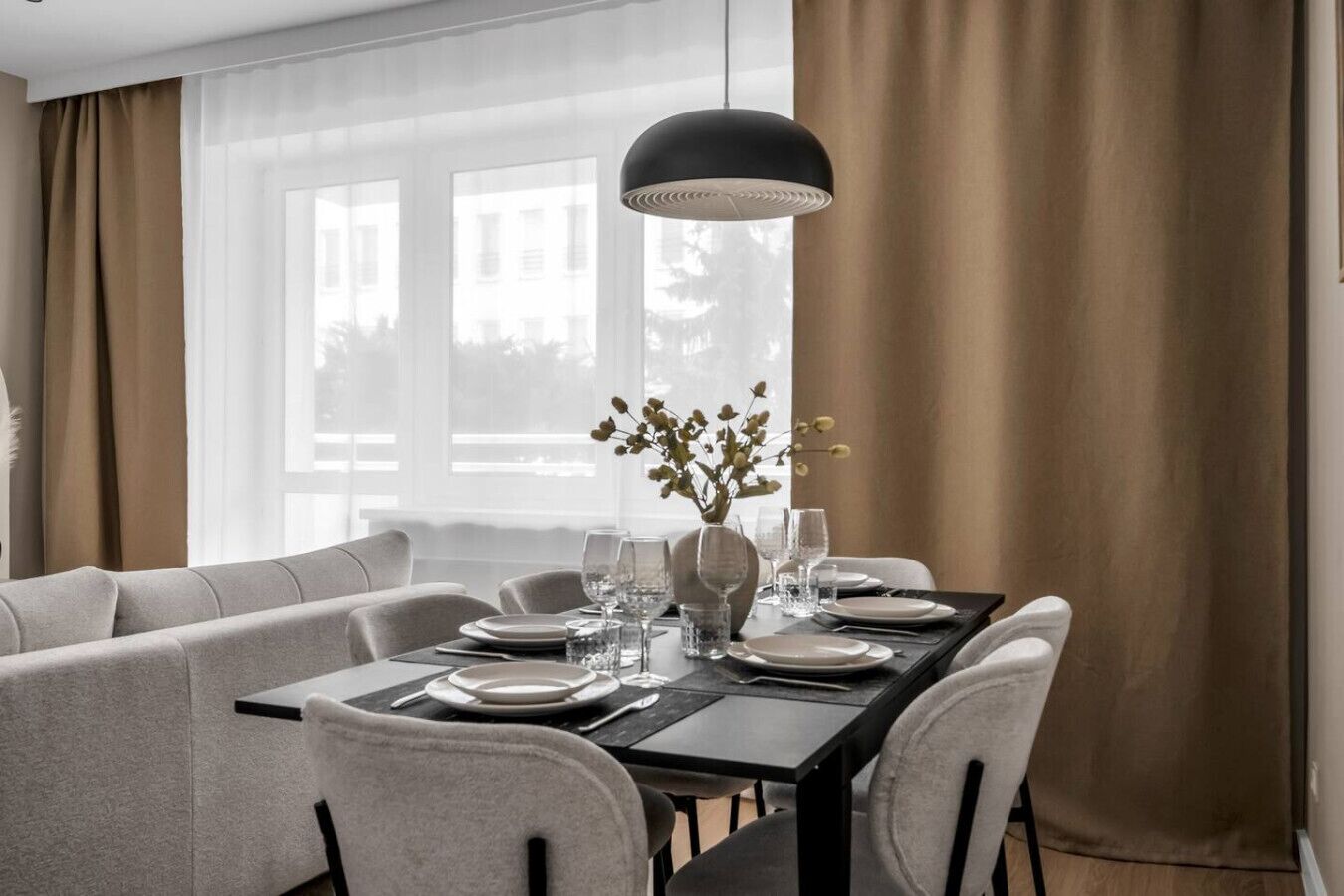A dining area with a rectangular table set for four, a vase with flowers, and a pendant light.