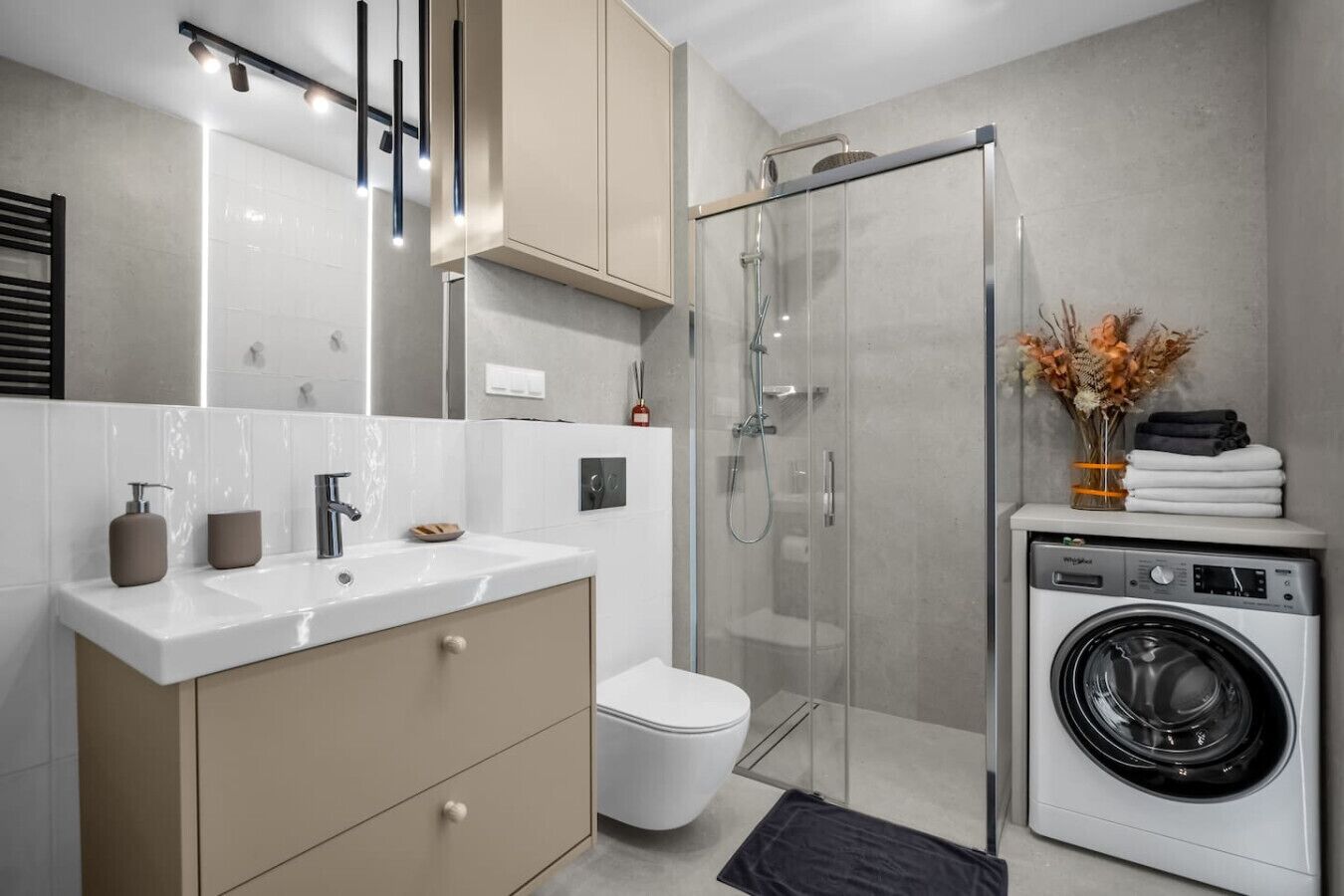 A modern bathroom with a glass shower enclosure, a built-in washing machine, and a vanity with a mirror.