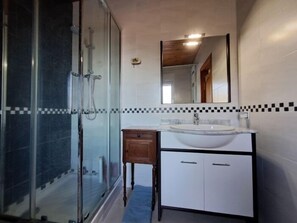 A bathroom with a glass shower enclosure, a sink with a mirror above, and tiled walls.