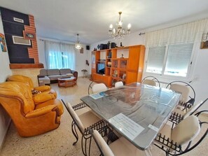 A living room with a sofa, a dining table with chairs, a TV, and a bookshelf.