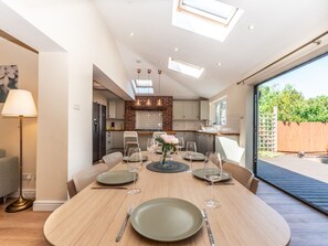 A modern kitchen with a skylight, a dining area with a round table, and a view of a garden through a glass door.