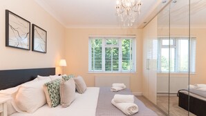 Une chambre à coucher avec un lit, une lampe de chevet, une fenêtre avec des stores et un lustre.