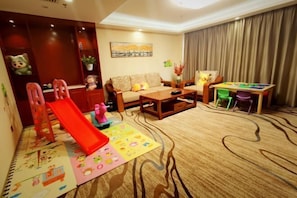 A living room with a sofa, a coffee table, a red slide, and a children's play mat. - Huachen Hotel (Lanzhou)