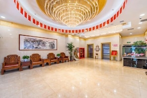A lobby with a chandelier, wooden chairs, a reception desk, and a framed artwork on the wall. - Huachen Hotel (Lanzhou)