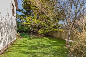 A well-maintained backyard with a lawn, a wooden fence, and a variety of trees.