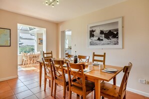 A dining area with a wooden table and chairs, a black and white photograph on the wall, and a view through an open door.