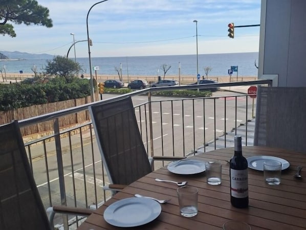 A table with plates, a wine bottle, and glasses on a balcony overlooking a street with cars and a view of the sea.