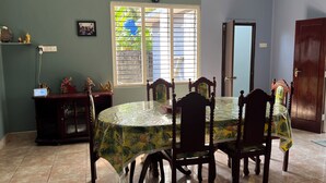 A dining area with a round table covered by a tropical leaf-patterned tablecloth, surrounded by wooden chairs.