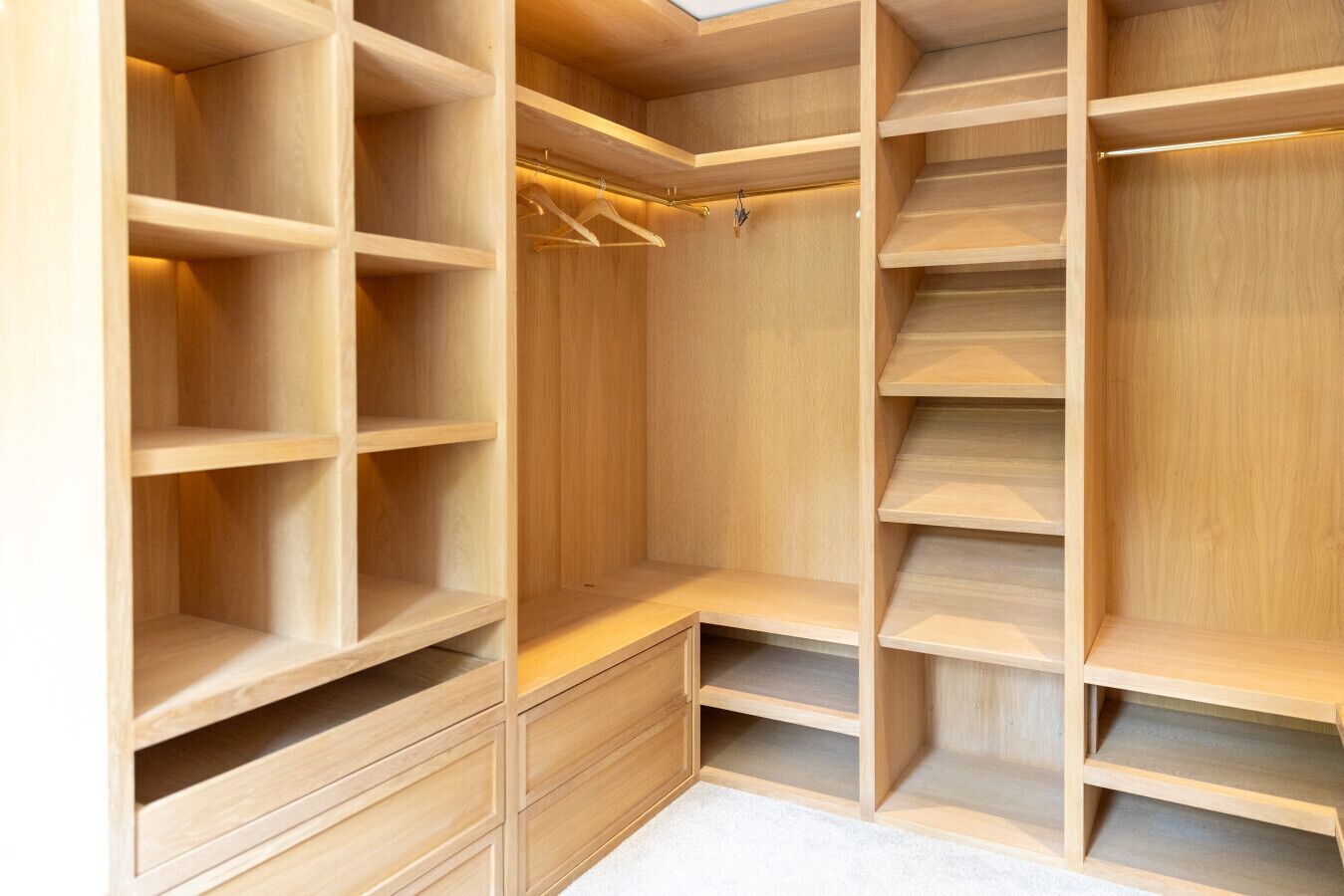 A wooden walk-in closet with multiple shelves, hanging space, and drawers.