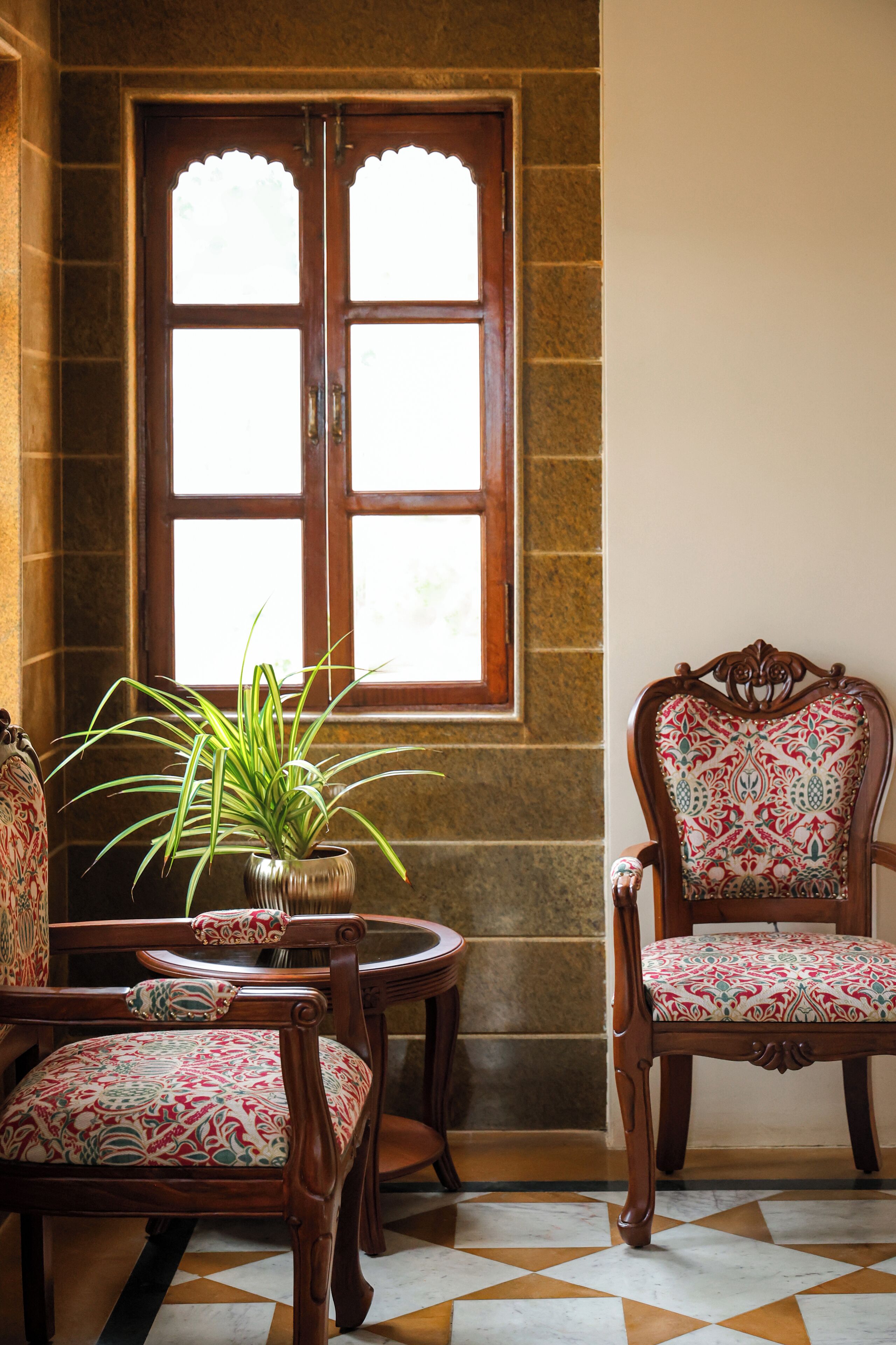 Una habitación con un ventanal grande, una planta en maceta y dos sillones con cojines estampados.