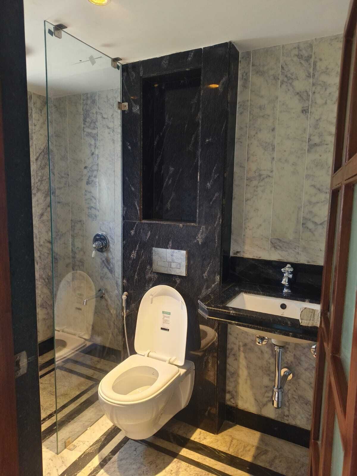 A modern bathroom with a glass-enclosed shower, a marble-tiled floor, a white toilet, and a black marble vanity with a sink.