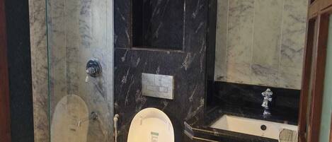 A modern bathroom with a glass-enclosed shower, a marble-tiled floor, a white toilet, and a black marble vanity with a sink.