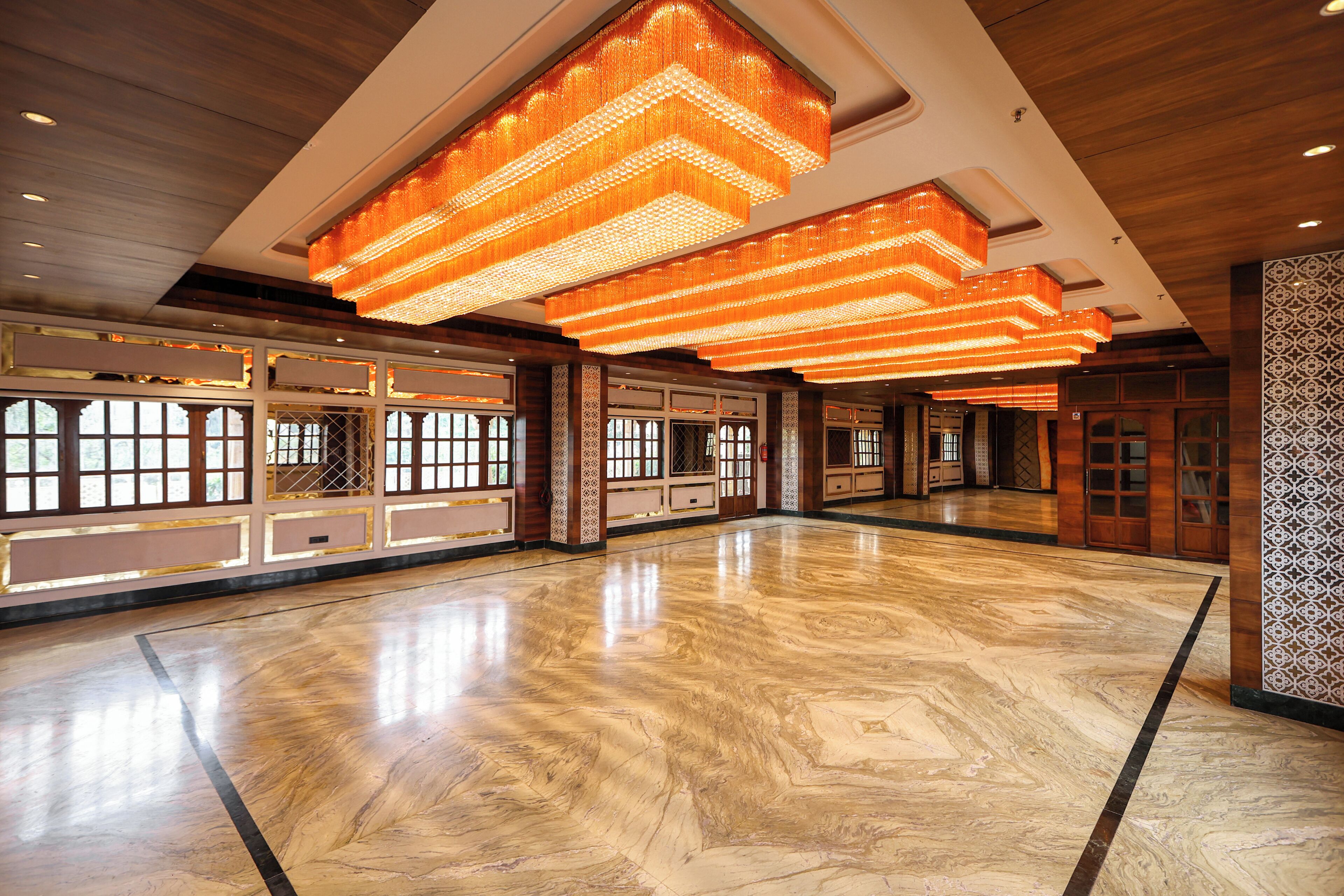 A spacious lobby with a polished marble floor, large wooden doors, and a modern chandelier.