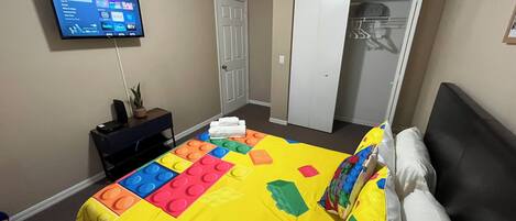 Una habitación de hotel con cama, televisión montada en la pared, escritorio con planta y armario.