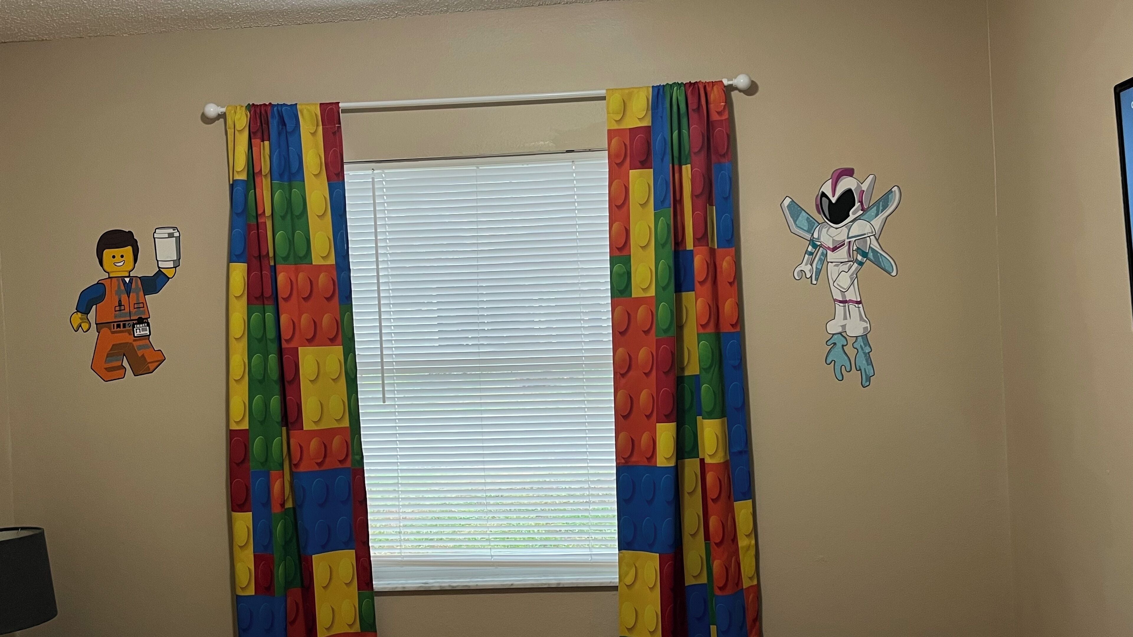 A room with a window covered by colorful curtains, a wall with a LEGO figure on the left and a character on the right.
