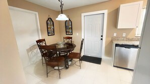 A dining area with a round table and chairs, a white door, a refrigerator, and wall-mounted decorations. - BlockHaven near Legoland & Disney (Winter Haven)