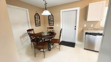 Uma sala de jantar com uma mesa redonda e cadeiras, uma porta branca, uma geladeira e decorações na parede.