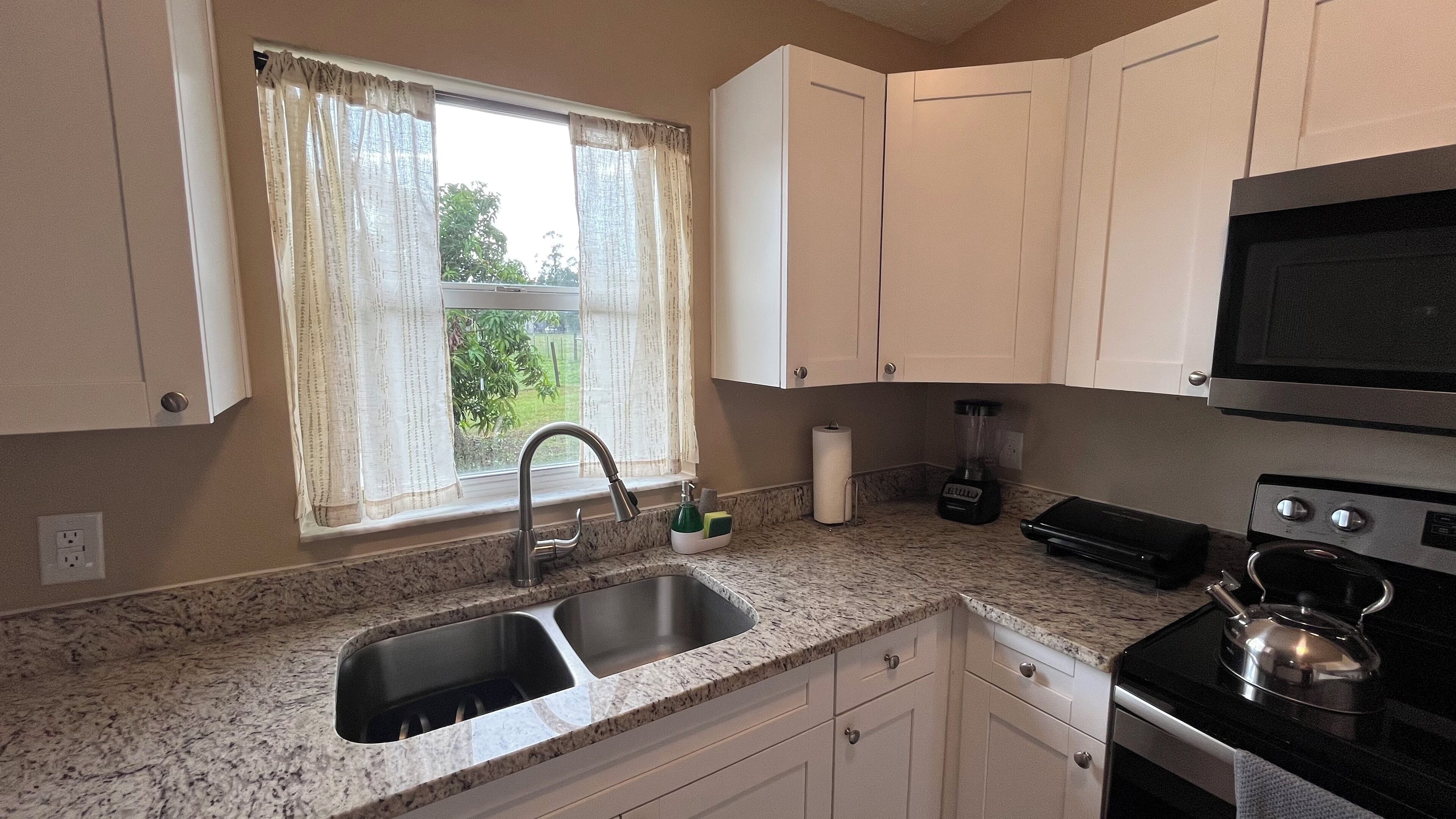 A kitchen with a double sink, a stove, a microwave, and a window with curtains.
