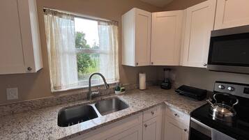 A kitchen with a double sink, a stove, a microwave, and a window with curtains.