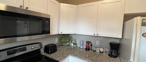 A compact kitchen with white cabinets, a stainless steel microwave, a stove, a toaster, and a coffee maker.