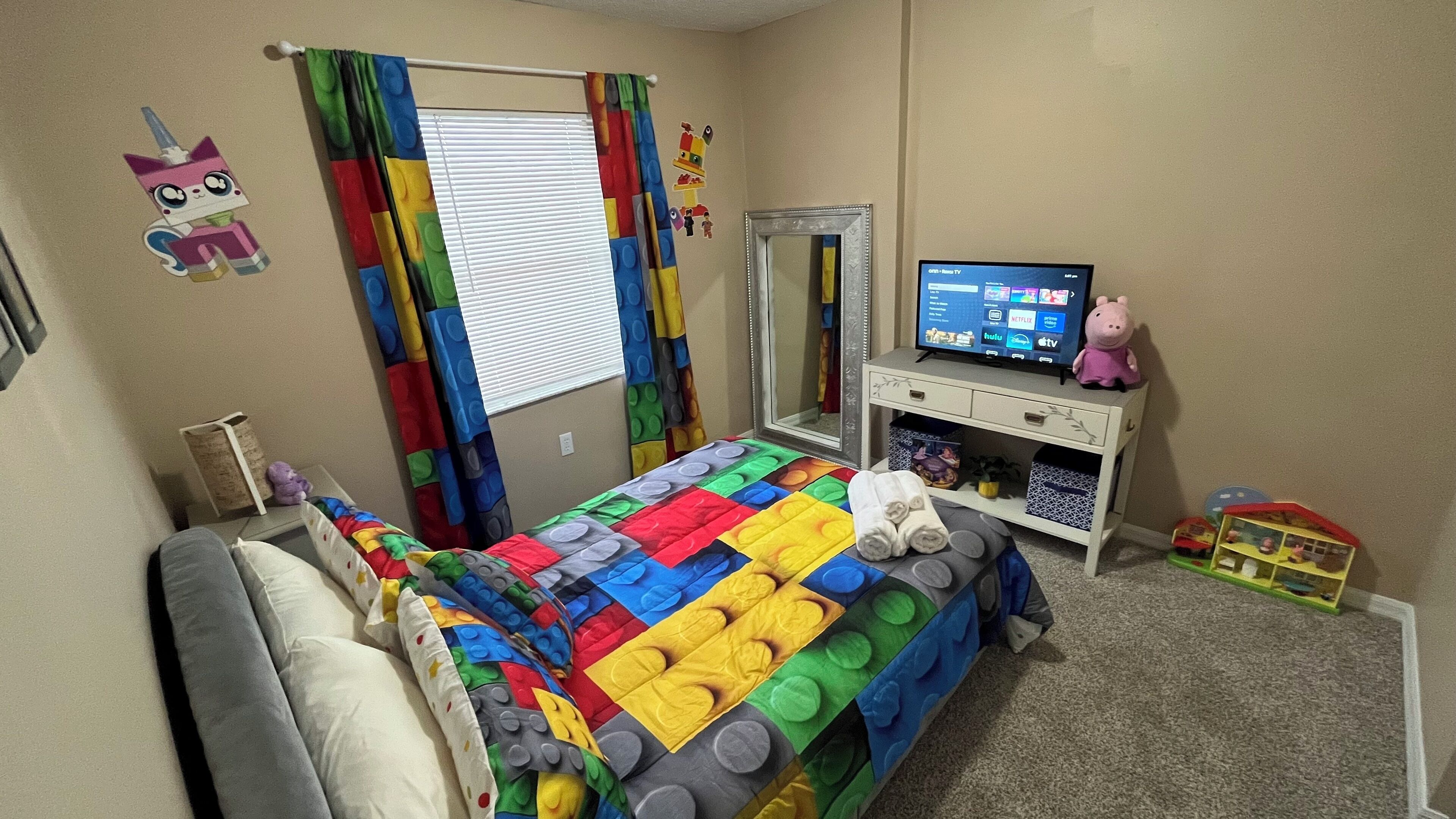 Un dormitorio con cama, televisor, cómoda y ventana con cortinas.